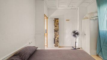 Un dormitorio con cama, ventilador y puerta que da a otra habitación.