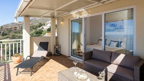A balcony with a chair, a sofa, a table, and a glass door leading to a bedroom. - Apartment M&K - Two Bedroom Apartment With Balcony and Sea View (Zupa dubrovacka)