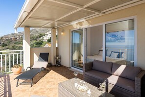 A balcony with a chair, a sofa, a table, and a glass door leading to a bedroom. - Apartment M&K - Two Bedroom Apartment With Balcony and Sea View (Zupa dubrovacka)