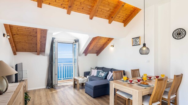 A spacious living area with a high ceiling, a balcony with a view, and a dining setup. - Apartment M&K - Two Bedroom Apartment With Balcony and Sea View (Zupa dubrovacka)