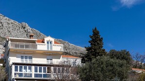 A two-story building with balconies, a mountain backdrop, and a clear sky. - Apartment M&K - Two Bedroom Apartment With Balcony and Sea View (Zupa dubrovacka)