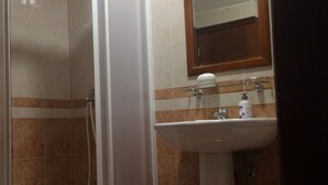 Un baño con ducha de vidrio, lavamanos con espejo y artículos de aseo sobre el lavamanos.