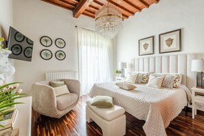 A bedroom with a bed, two nightstands, a chair, a small table, and a chandelier. - The Tuscan Serenade in Lucca (Lucca)