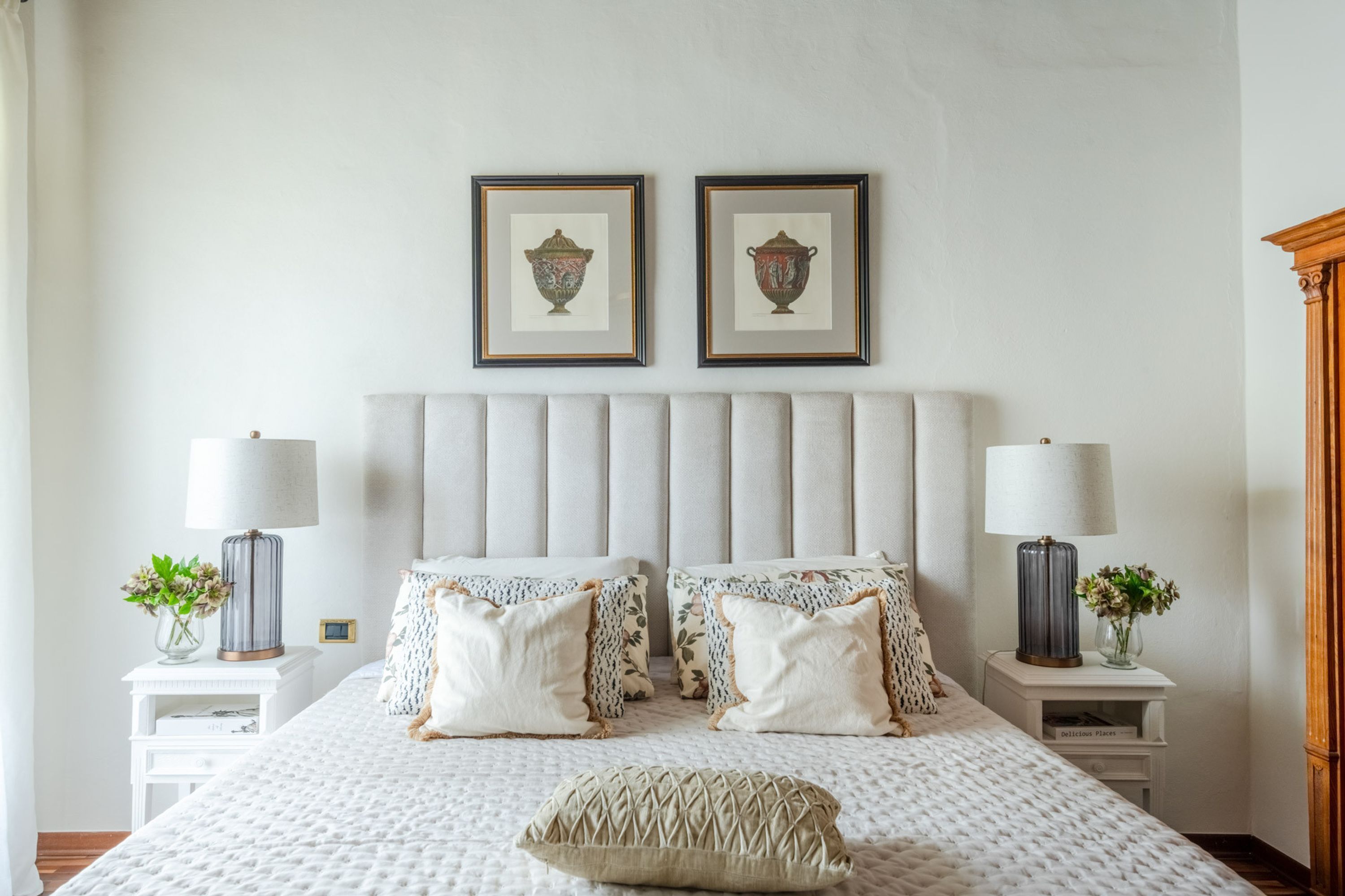 A bedroom with a large bed, two nightstands, a wooden wardrobe, and two framed pictures on the wall.
