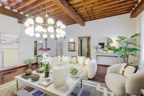 A modern living room with a wooden ceiling, a chandelier, a sofa set, and a coffee table with books and decorative items. - The Tuscan Serenade in Lucca (Lucca)