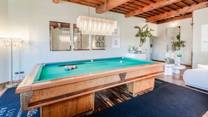 A pool table in a room with wooden beams, a hanging light fixture, and framed pictures on the wall. - The Tuscan Serenade in Lucca (Lucca)