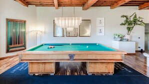 A pool table with a wooden frame, a hanging light fixture, and a potted plant on a white pedestal. - The Tuscan Serenade in Lucca (Lucca)