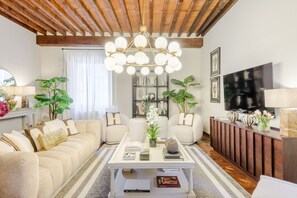 A living room with a sofa, coffee table, and a TV. There are plants and books on shelves. - The Tuscan Serenade in Lucca (Lucca)