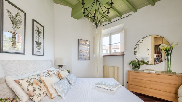 A bedroom with a large bed, a dresser, a mirror, and artwork on the walls. - The Tuscan Serenade in Lucca (Lucca)