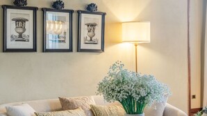 A living room with a sofa, a vase with flowers, a lamp, and framed pictures on the wall. - The Tuscan Serenade in Lucca (Lucca)