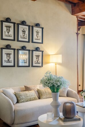 Ein Wohnzimmer mit einer Couch, einer Blumenvase, einer Lampe und gerahmten Bildern an der Wand.