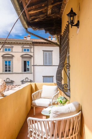 Un balcon agrémenté de meubles en osier, d’une petite table et d’une applique murale décorative.