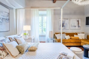 A bedroom with a large bed, a sofa, a window with curtains, and artwork on the walls. - The Tuscan Serenade in Lucca (Lucca)