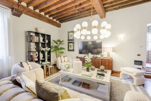 A living room with a sofa, coffee table, bookshelf, and a TV. - The Tuscan Serenade in Lucca (Lucca)