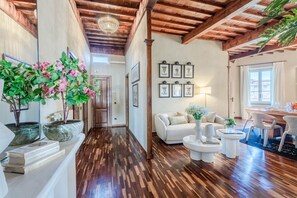 A spacious living area with a wooden floor, a white sofa, a coffee table, and a dining area with chairs. - The Tuscan Serenade in Lucca (Lucca)