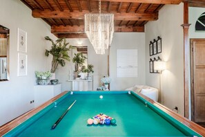 A pool table with balls, a chandelier, and a mirror in a room with wooden beams and framed pictures on the walls. - The Tuscan Serenade in Lucca (Lucca)