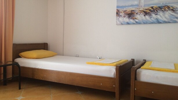 Un letto singolo con struttura in legno e materasso bianco, un cuscino giallo e un quadro raffigurante un faro appeso al muro.