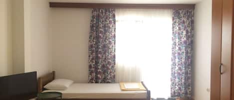 A hotel room with a single bed, a desk with a computer, a television, and a wardrobe.