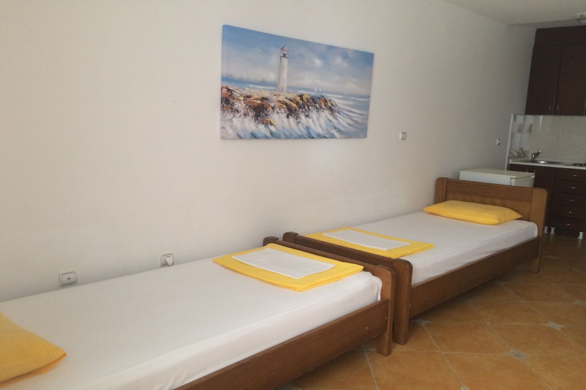 Ein Zimmer mit zwei Einzelbetten, einer kleinen Küchenzeile und einem Gemälde eines Leuchtturms an der Wand.