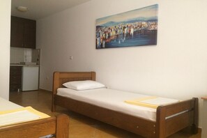 A single bed with a wooden frame and white bedding in a small room with a kitchenette and a painting on the wall. - Apartments Aleksić, Bečići - Studio Apartment with Terrace 1 (Becici)