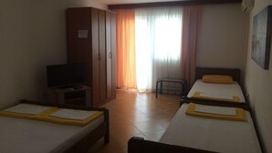 Ein Hotelzimmer mit zwei Einzelbetten, einem Fernseher, einem Kleiderschrank und einem Sessel.