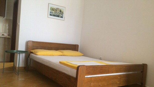 Ein Einzelbett mit Holzrahmen und gelber Bettwäsche in einem Zimmer mit Fliesenboden.