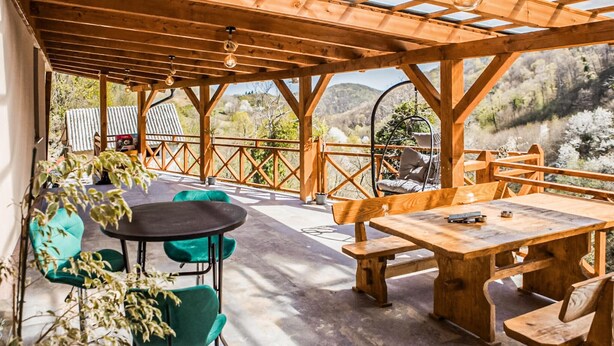 Een terras buiten met houten meubels, waaronder een tafel en bankjes, met uitzicht op een bergachtig landschap.