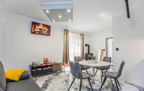 A modern living room with a fireplace, a round dining table with chairs, a sofa with a yellow cushion, and a television mounted on the wall. - Beautiful home in Lepoglava with WiFi (Lepoglava)