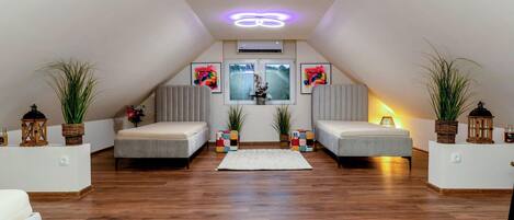 A modern loft bedroom with a sloped ceiling, two beds, a large window, and a central light fixture.