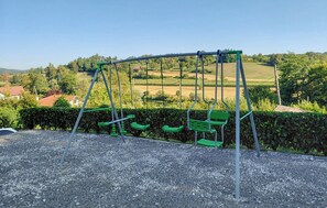 Spielplatz mit Schaukeln in einem Kiesbereich, Blick auf eine ländliche Gegend.