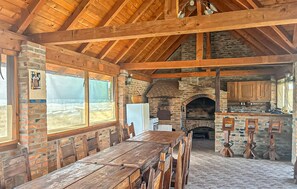 A rustic dining area with a wooden table and chairs, a brick wall, and a stone fireplace.