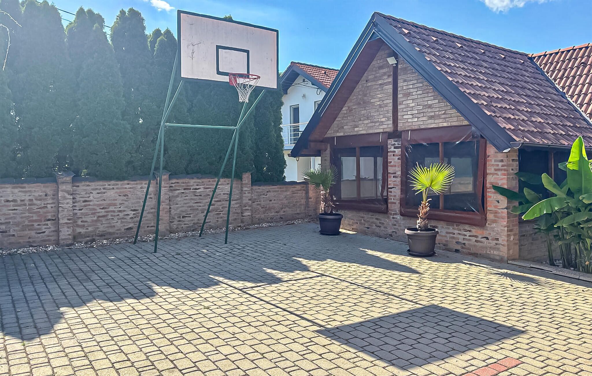 Un espace extérieur aménagé avec un revêtement pavé, un panier de basket, des plantes en pot et un bâtiment en briques.