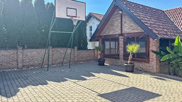 Un espace extérieur aménagé avec un revêtement pavé, un panier de basket, des plantes en pot et un bâtiment en briques.