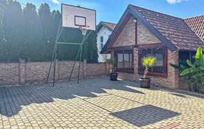 A paved outdoor area with a basketball hoop, potted plants, and a brick building.