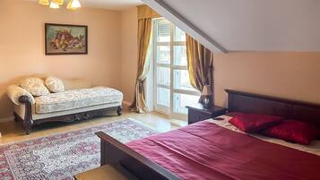 A bedroom with a bed, a sofa, a nightstand, a lamp, a window with curtains, and a painting on the wall.