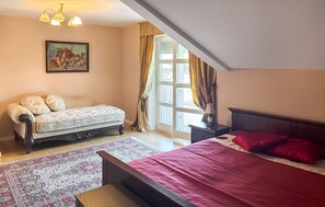 A bedroom with a bed, a sofa, a nightstand, a lamp, a window with curtains, and a painting on the wall.