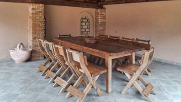 A rustic outdoor dining area with a wooden table and chairs, a brick wall, and a tiled floor.