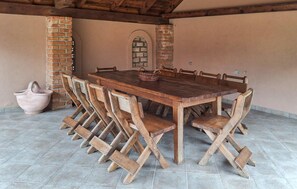 A rustic outdoor dining area with a wooden table and chairs, a brick wall, and a tiled floor.