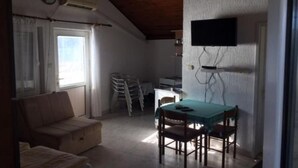 Ett litet, kompakt rum med ett träpanelat tak, en soffa, ett matbord med stolar, en tv som är monterad på väggen och ett fönster med gardiner.