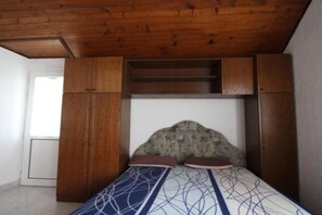 Ein Schlafzimmer mit Holzboden, einem Bett mit gemusterten Betttextilien und eingebauten Holzschränken.