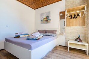 Ein modernes Schlafzimmer mit einem Bett, Holzboden, einem Gemälde, einem Kleiderhaken und einem kleinen Tisch mit einer Weinflasche.
