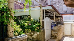 Une ruelle étroite bordée d’un mur de pierre, un petit jardin agrémenté d’hortensias et un bâtiment sur lequel on peut lire l’inscription « 7 U PILAMA » ainsi que les mots « Rooms, Zimmer, Chambre, Camere ».