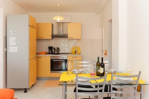 Eine kompakte Küche mit Essbereich, ausgestattet mit einem Kühlschrank, Backofen und einem für zwei Personen gedecktem Esstisch.