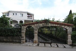 A gated entrance with stone arches, a white building with balconies in the background, and greenery around. - Apartments Roza - One bedroom apartment with Garden view (Herceg Novi)