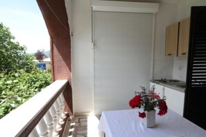 A balcony with a closed white door, a small table with a white tablecloth, and a vase with red flowers. - Apartments Roza - One bedroom apartment with Garden view (Herceg Novi)