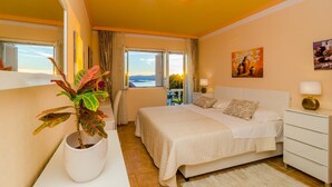 Una camera d'albergo con un letto, una pianta in vaso, un quadro e vista sul mare.