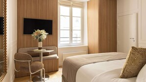 A hotel room with a bed, a seating area with a chair, a television, and a wardrobe. - Sublime Suite Saint Honore, Elysee Palace (Paris)