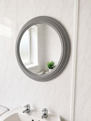 Une salle de bain avec un grand miroir rond, des murs en marbre blanc et un lavabo doté de deux robinets.