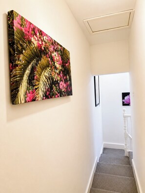 A hallway with a staircase, a wall-mounted painting, and a door at the end.
