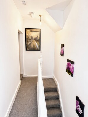 Un escalier orné d’une affiche représentant un paysage urbain, d’un luminaire et de deux tableaux floraux.